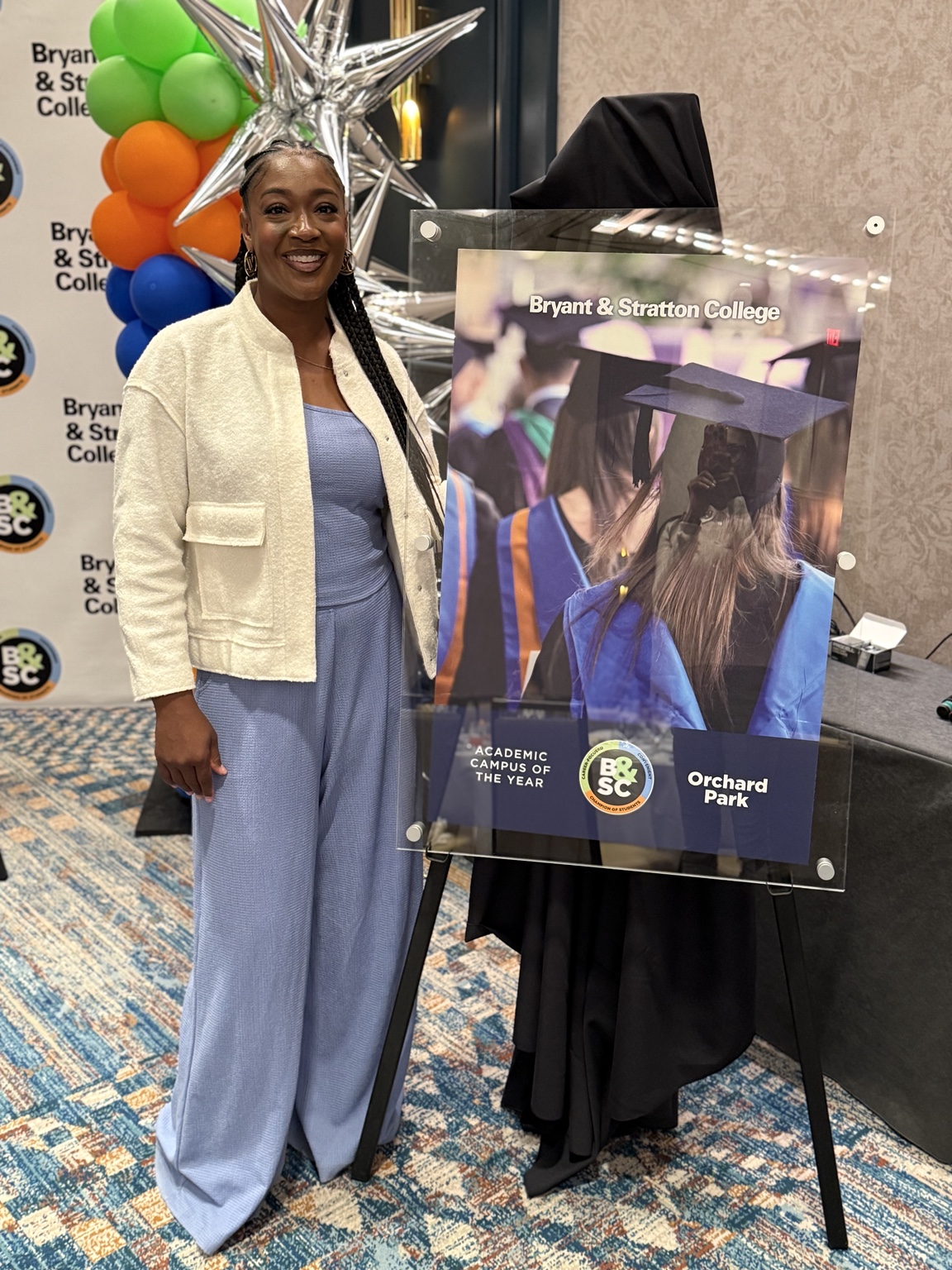 Dr. Danielle Tucker standing beside the Bryant & Stratton College Orchard Park Academic Campus of the Year award display